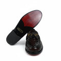 A dark brown embossed leather loafer shown from the side, with its sole lifted to reveal a black outsole and a red-painted heel counter, set against a white fabric backdrop.