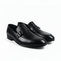 A pair of black leather penny loafers with a decorative strap and silver buckle, displayed on a light gray surface.