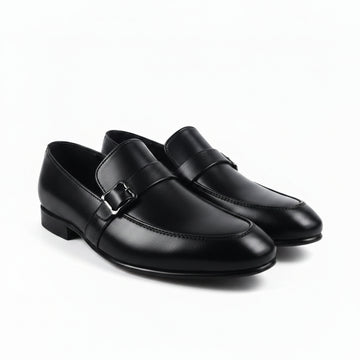 A pair of black leather penny loafers with a decorative strap and silver buckle, displayed on a light gray surface.