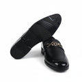 A pair of black leather penny loafers with a gold-tone double-G buckle detail, shown on a white studio background with one shoe turned to display the sole.