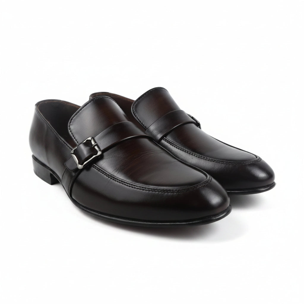 A pair of dark brown leather slip-on loafers with a single strap and a silver-tone buckle, displayed on a light gray background.