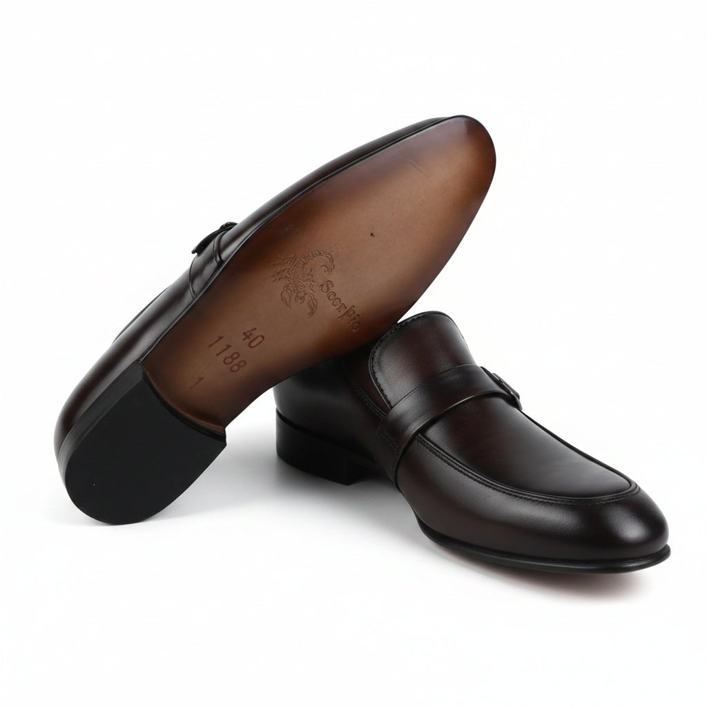 A pair of dark brown leather penny loafers, with one shoe standing upright to show the brown outsole and the other lying flat to show the top, set against a plain white background.