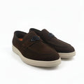 A pair of men's brown suede slip-on loafers with a decorative metal logo detail on the vamp and thick cream-colored soles, displayed against a white studio background.