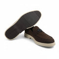 A pair of dark brown suede loafers with cream-colored soles, with one shoe turned to show the textured black outsole. A small black metal logo is visible on the side of the shoe.