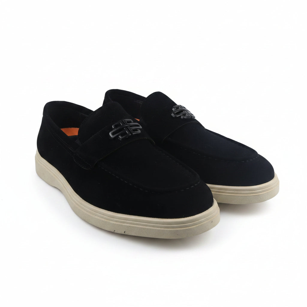 A pair of black slip-on loafers with a textured strap across the instep and beige soles, photographed on a white studio background.