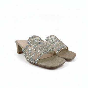 A pair of women's heeled slide sandals with glittery beige soles and straps heavily embellished with clear rhinestones and pearl-like accents, set against a plain light gray backdrop.