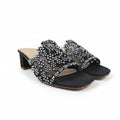 A pair of black open-toe heeled slide sandals embellished with rows of clear rhinestones across the straps, shown on a white studio floor.