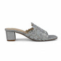 A single silver glitter mule sandal with intricate rhinestone embellishments across the strap, set against a light gray fabric backdrop.