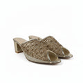 A pair of women's heeled mule sandals with a textured metallic gold woven upper and a chunky block heel, shown on a light gray fabric background.