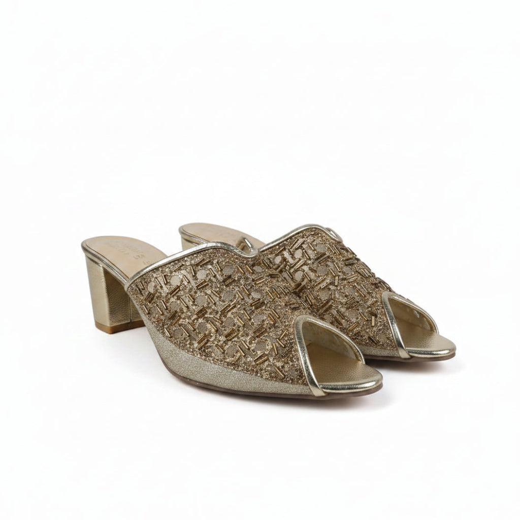 A pair of women's heeled mule sandals with a textured metallic gold woven upper and a chunky block heel, shown on a light gray fabric background.
