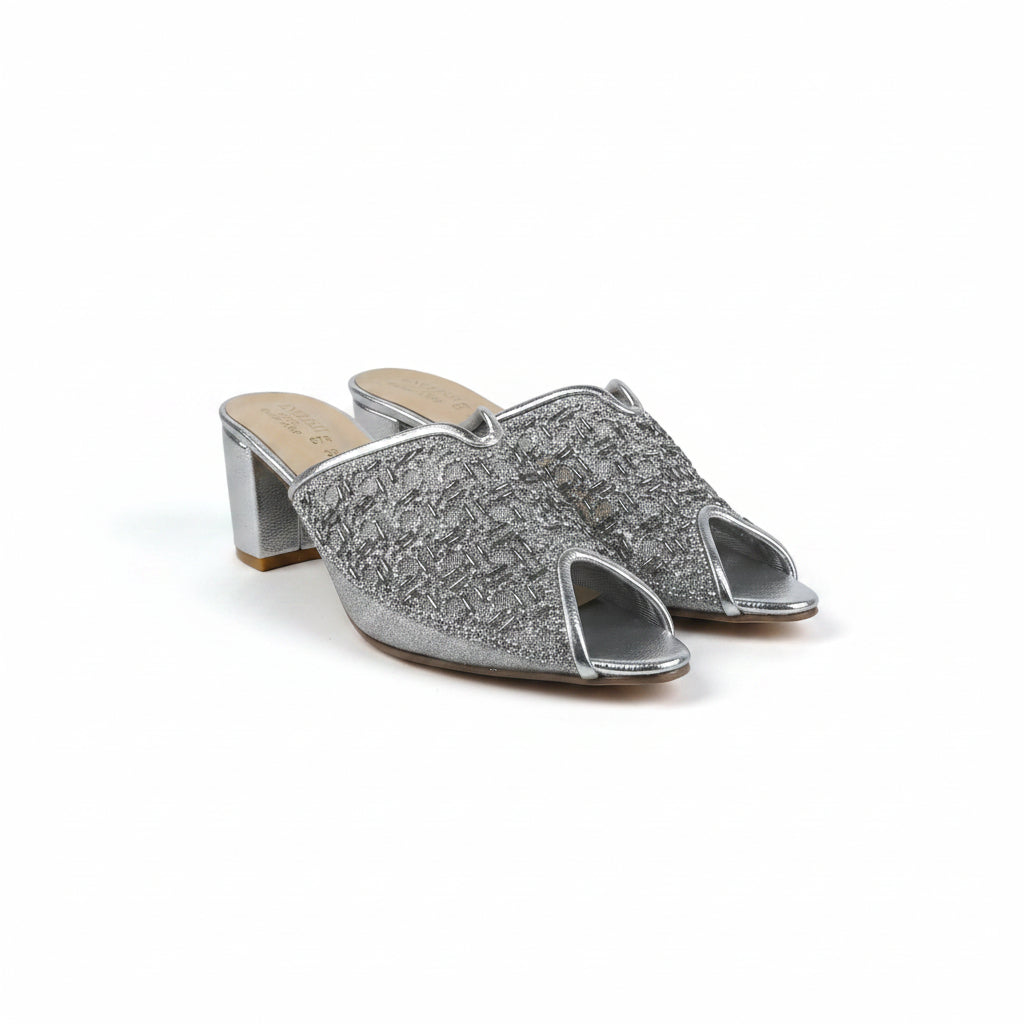 A pair of women's open-toe mule heels with chunky block heels, featuring a textured silver glitter upper and a light beige insole, photographed on a white studio background.