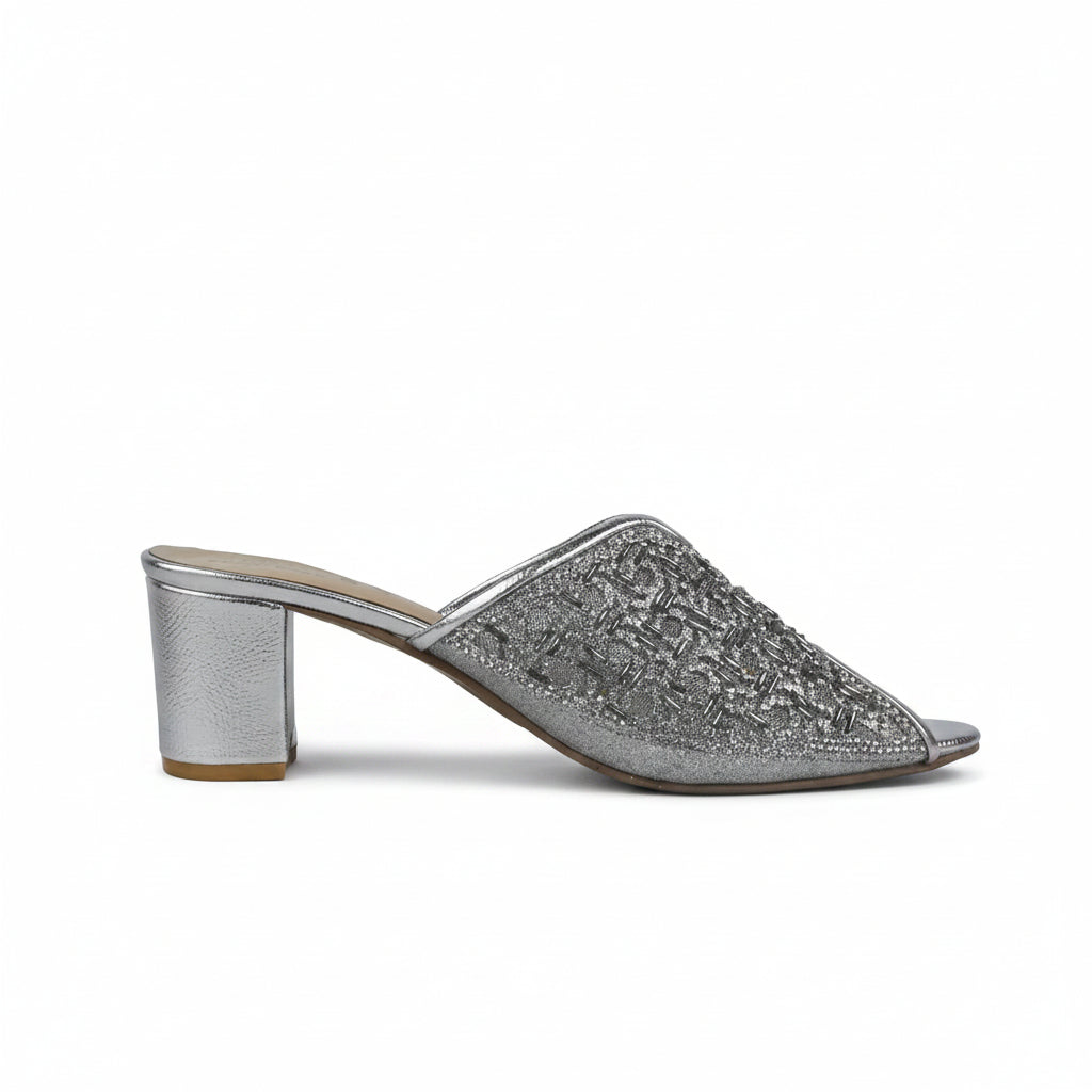 A single silver glitter mule sandal with a block heel, shown from the side against a light gray textured background.