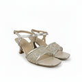 A pair of women's heeled sandals in a metallic champagne gold color, featuring an open toe, a square toe cap, and a thin ankle strap with a buckle closure. The straps are embellished with a textured, glittery pattern, and the insole is a light beige nude color.
