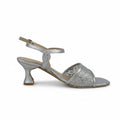 A single silver glitter heeled sandal with an ankle strap and open toe, shown from the side against a light gray textured background.