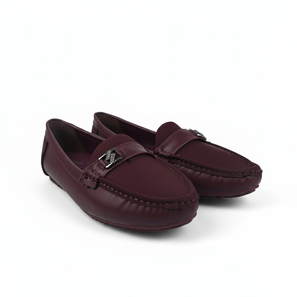 A pair of women's burgundy leather driving loafers with a small silver-tone metal logo charm on the strap, displayed on a light gray studio background.