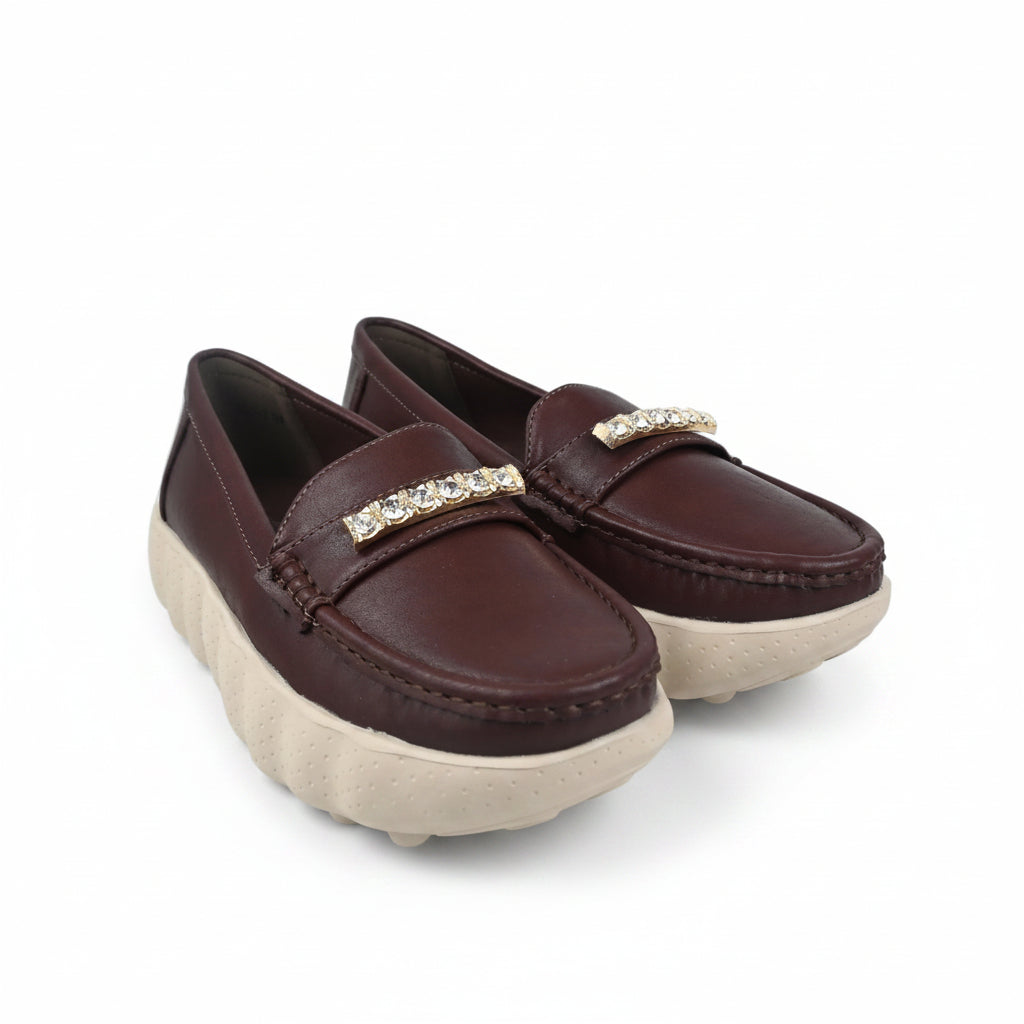 A pair of women's slip-on loafers in dark burgundy brown leather, featuring a decorative gold-tone rhinestone-embellished strap and chunky off-white platform soles, shown on a white studio background.