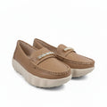 A pair of tan slip-on loafers with a decorative gold-tone embellished strap and chunky off-white platform soles, photographed on a white studio floor.