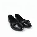 A pair of black patent leather ballet flats with a pointed toe and a decorative crisscross strap across the instep, displayed on a white studio floor.