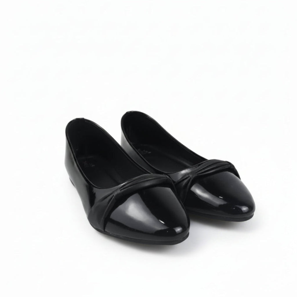 A pair of black patent leather ballet flats with a pointed toe and a decorative crisscross strap across the instep, displayed on a white studio floor.