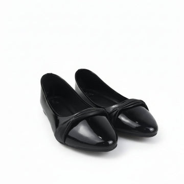 A pair of black patent leather ballet flats with a pointed toe and a decorative crisscross strap across the instep, displayed on a white studio floor.