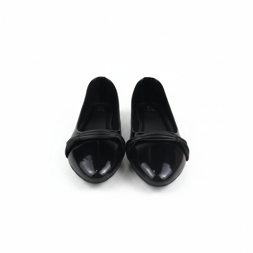 A pair of black patent leather ballet flats with a pointed toe and a decorative crisscross strap across the instep, displayed on a white studio floor.