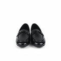 A pair of black patent leather loafers with a decorative strap and buckle detail across the vamp, displayed on a white surface with a brown cardboard box partially visible on the right.