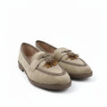 A pair of beige suede tassel loafers with brown trim and soles, displayed on a white studio background.