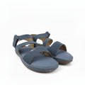 A pair of women's flat sandals in a muted slate blue color, featuring textured straps and a low wedge heel, photographed on a white studio background.