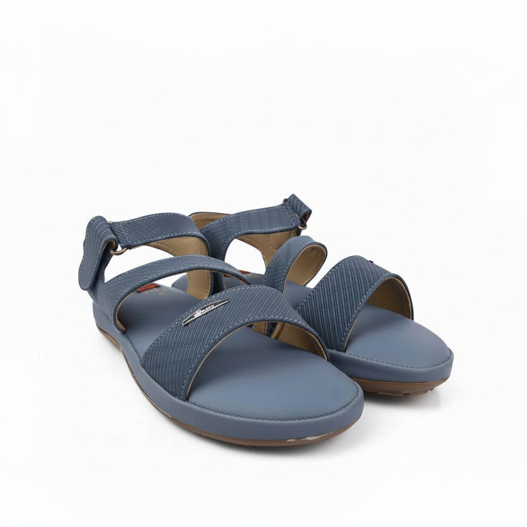 A pair of women's flat sandals in a muted slate blue color, featuring textured straps and a low wedge heel, photographed on a white studio background.