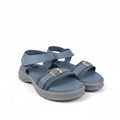 A pair of women's casual sandals in a muted slate blue color, featuring double straps with gold-tone buckle details and a thick gray sole, set against a plain light gray background.