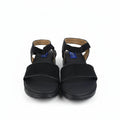 A pair of black slide sandals with wide straps and ankle bands, shown from the front on a white studio background.