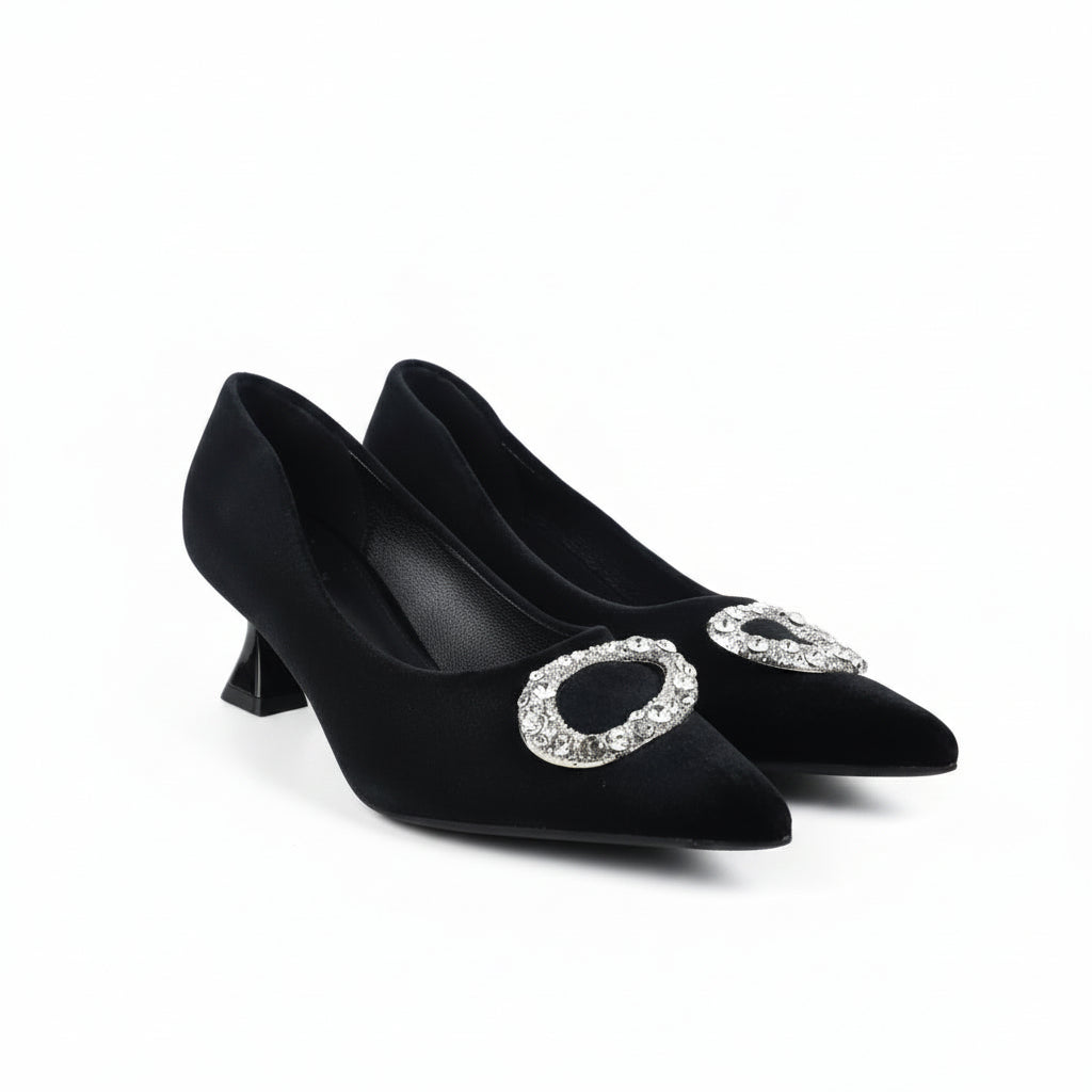 A pair of black pointed-toe kitten heels with large oval silver rhinestone embellishments on the front, photographed on a white studio floor.