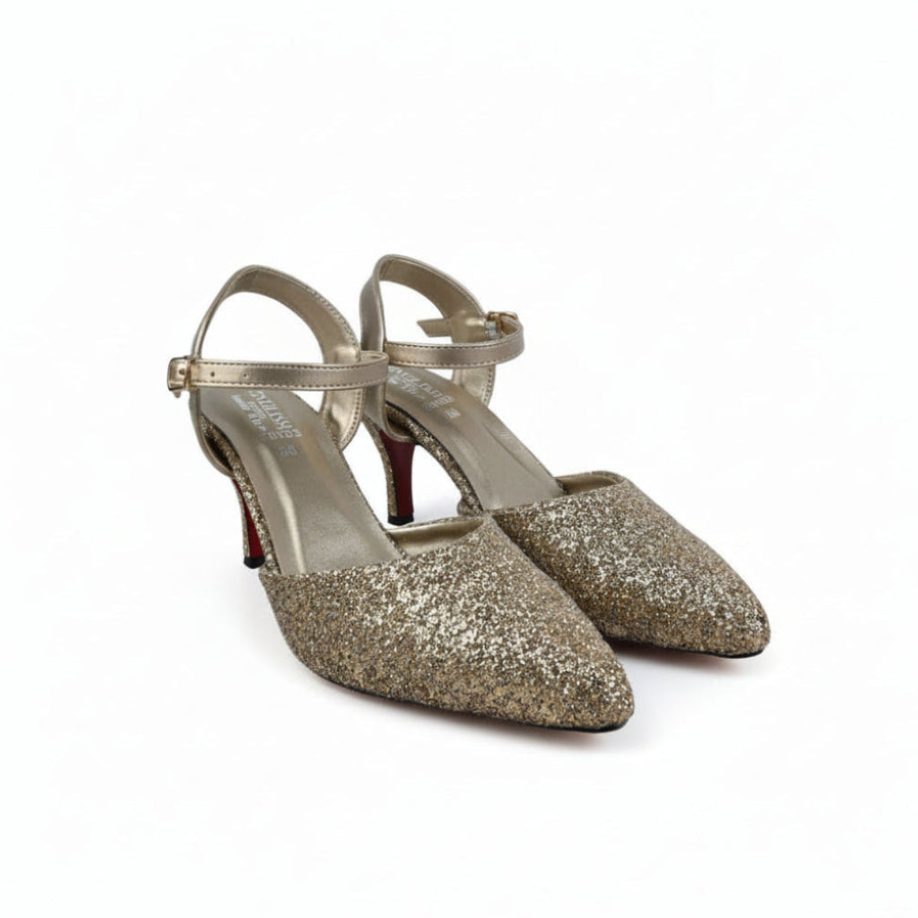 A pair of pointed-toe high heels covered in gold glitter, featuring gold ankle straps and red low-profile heels, photographed on a white studio background.