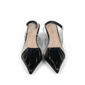A pair of pointed-toe slingback heels with glossy black patent leather caps and clear transparent straps, shown on a light gray surface with a partial orange box visible on the right.