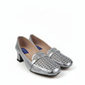 A pair of metallic silver kitten heels with woven textured detailing across the vamp, displayed on a light gray fabric backdrop.