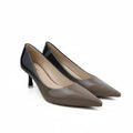 A pair of pointed-toe kitten heel pumps in a glossy taupe-brown patent leather, displayed on a white studio floor with a black power cord and studio equipment visible.