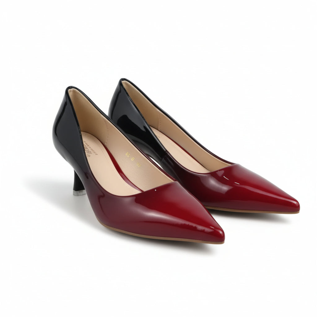 A pair of pointed-toe mid-height pumps with a glossy two-tone finish, featuring a black back and a deep red front, displayed on a light gray floor.