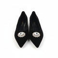 A pair of black pointed-toe high heels with ornate silver-tone and crystal embellishments on the toes, shown next to their orange and black shoebox on a white background.