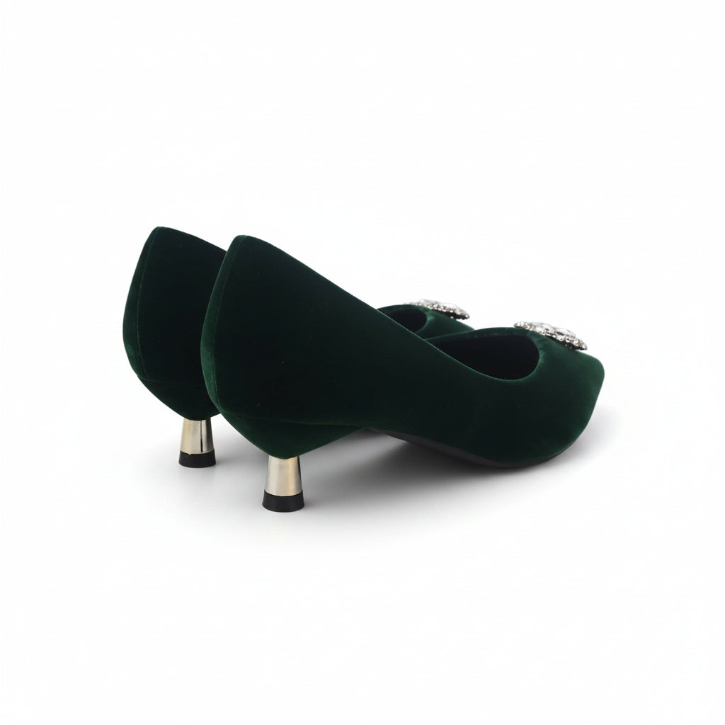 A pair of dark green velvet pointed-toe pumps with metallic gold heels and small silver rhinestone embellishments on the sides, photographed on a white studio background.