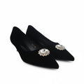 A pair of black pointed-toe kitten heels with jeweled floral embellishments on the toes, photographed on a white studio background.