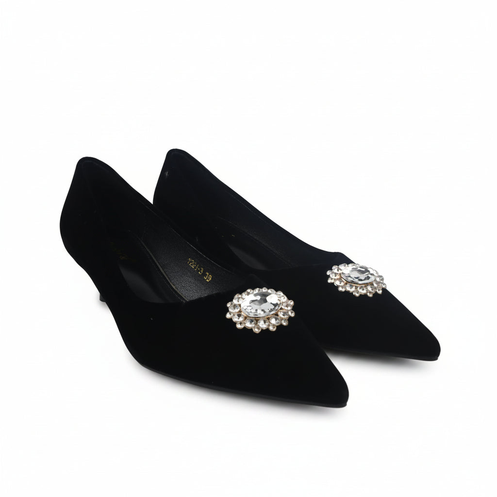 A pair of black pointed-toe kitten heels with jeweled floral embellishments on the toes, photographed on a white studio background.