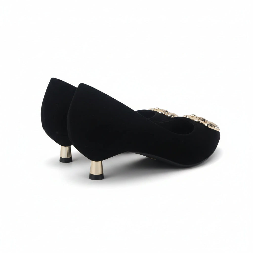 A pair of black velvet pointed-toe pumps with gold metallic heels and jeweled embellishments on the toe, set against a plain white background.