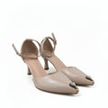 A pair of beige pointed-toe high heels with ankle straps and metallic gold toe caps, photographed on a light gray studio floor.