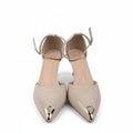 A pair of beige pointed-toe high heels with ankle straps and metallic gold toe caps, shown on a light gray surface with a shoebox partially visible on the right.