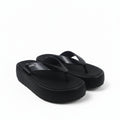 A pair of black platform flip-flops with thick straps, photographed on a white studio background with a black power cord visible in the lower left.
