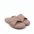 A pair of women's slide sandals in a dusty pink color, featuring a small gold-tone metal logo plaque on the strap, set against a white studio backdrop.