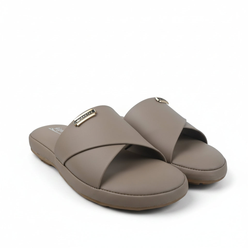 A pair of women's slide sandals in a dusty pink color, featuring a small gold-tone metal logo plaque on the strap, set against a white studio backdrop.
