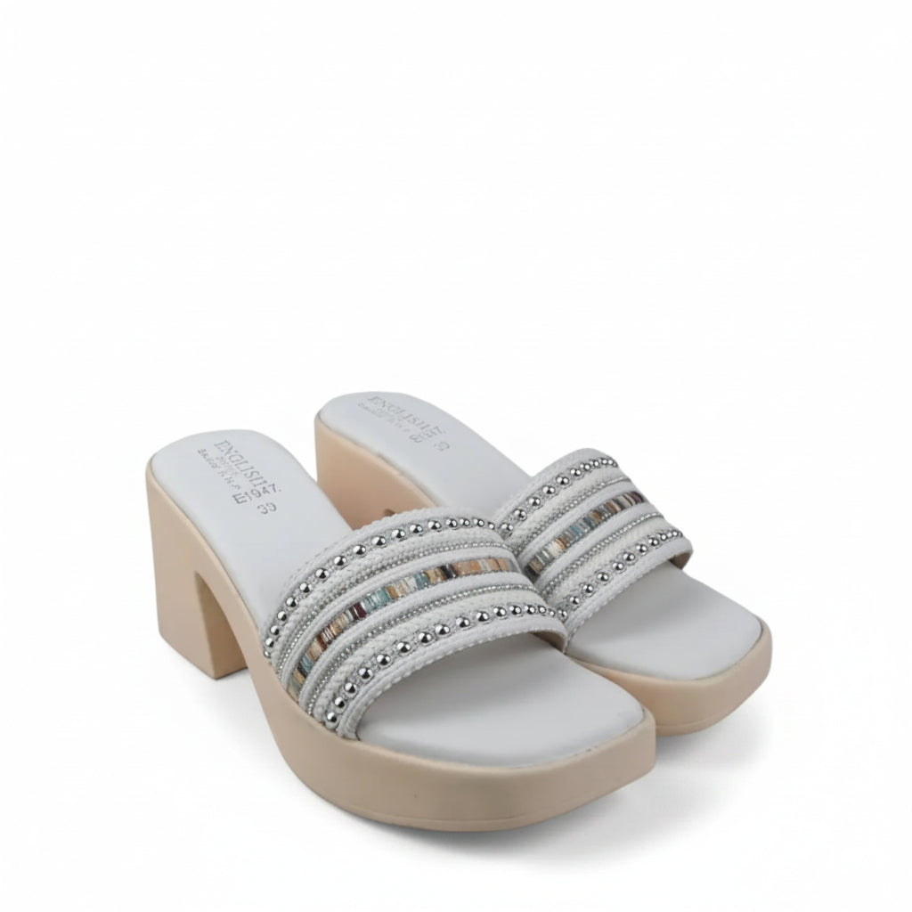 A pair of women's platform mule sandals with beige heels and white uppers, featuring multiple horizontal straps embellished with silver rhinestones, set against a white fabric backdrop.