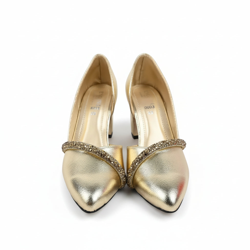 A pair of metallic gold pointed-toe high heels with a rhinestone-embellished cross-strap, displayed on a white studio floor.