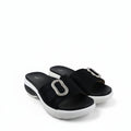 A pair of black platform slide sandals with a prominent silver-tone rectangular buckle embellished with clear rhinestones, shown on a white fabric backdrop.